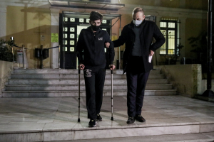 Φουρθιώτης με μάσκα, φόρμα, πατερίτσες και υποβασταζόμενος στον Εισαγγελέα